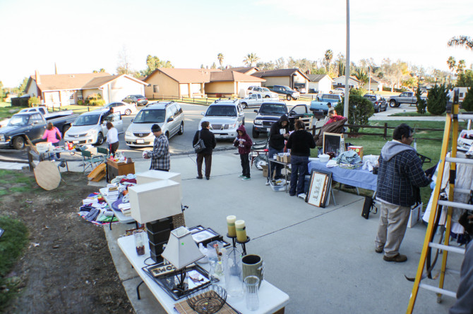 Garage sale with lots of cars and people buying everything